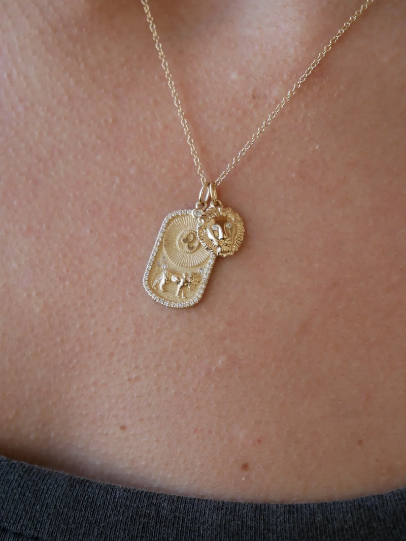 Close-up of the ef collection Gold and Diamond Lion Charm necklace—layered over a dark shirt, secured by an enhancer clasp, featuring a circular lion face pendant and a rectangular intricate charm.