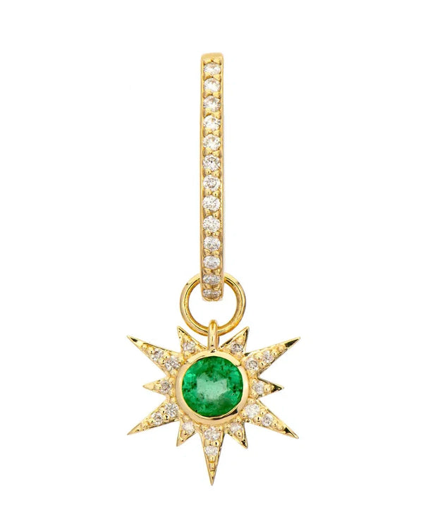 The Tiny Love Explosion Emerald Charms by Three Stories Jewelry feature a sunburst design with a central green gemstone, white topaz accents, and dangle from a 14K yellow gold diamond-studded hoop.