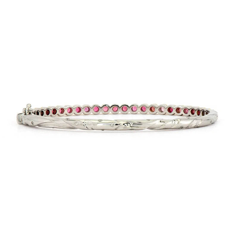 The Hammered Tourmaline Bezel Bangle by Three Stories Jewelry is a silver bracelet with a twisted design, showcasing pink gemstones along its inner side and elegantly accented with 14k yellow gold for a mixed metal allure.