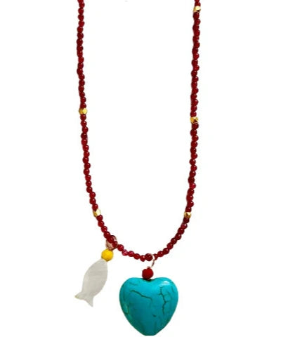 The Alora Turquoise Heart Necklace by Oiya features small red and gold beads, a large turquoise heart pendant, and a delicate mother of pearl fish charm.