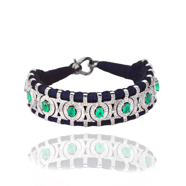 The Van Den Abeele Sao Paulo Black and Emeralds bracelet features emeralds set in a detailed silver and navy band with circular and geometric patterns, beautifully highlighted by the reflective surface on a white background.