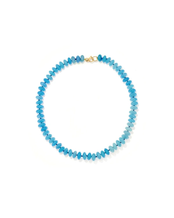 The Adina Reyter Coastal Blue Gemstone Necklace is a limited edition piece featuring round turquoise-hued beads and a gold clasp, beautifully arranged in a circle on a white background.