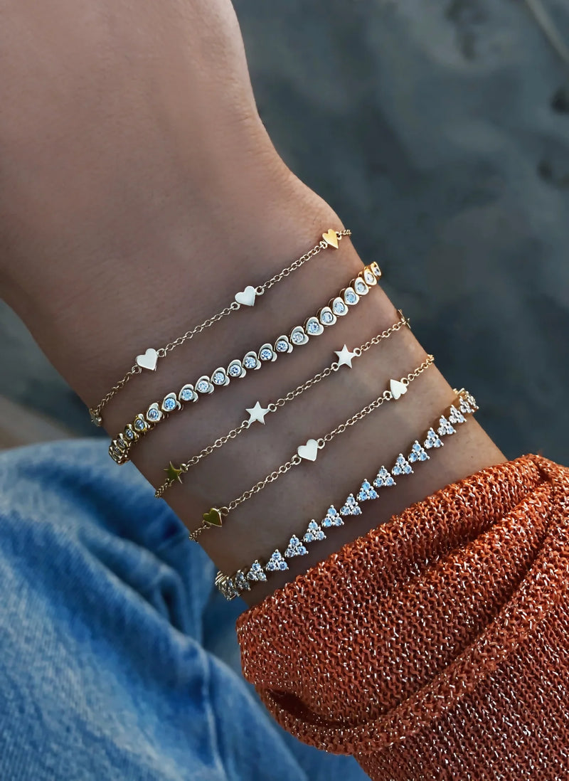 A wrist adorned with the Luna Skye 14kt gold full three diamond cluster tennis bracelet gleams against blue jeans and an orange textured sleeve, adding a touch of sparkle and elegance.