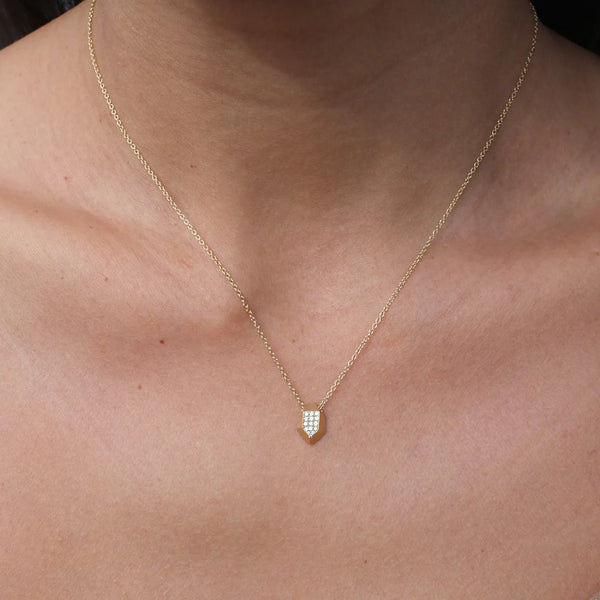 A close-up shows a person wearing the Elisabeth Bell Herkimer Necklace, featuring a delicate gold chain with a geometric pendant encrusted with tiny gemstones, resting on their collarbone. The blurred background emphasizes this exquisite piece of handmade jewelry.