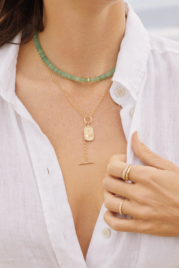 A woman wears a white button-up shirt, green beaded choker, gold rings, and gently holds her collar. Around her neck is the ef collection Rolo Chain Enhanced Lariat Necklace in 14k yellow gold, paired with a gold chain necklace.