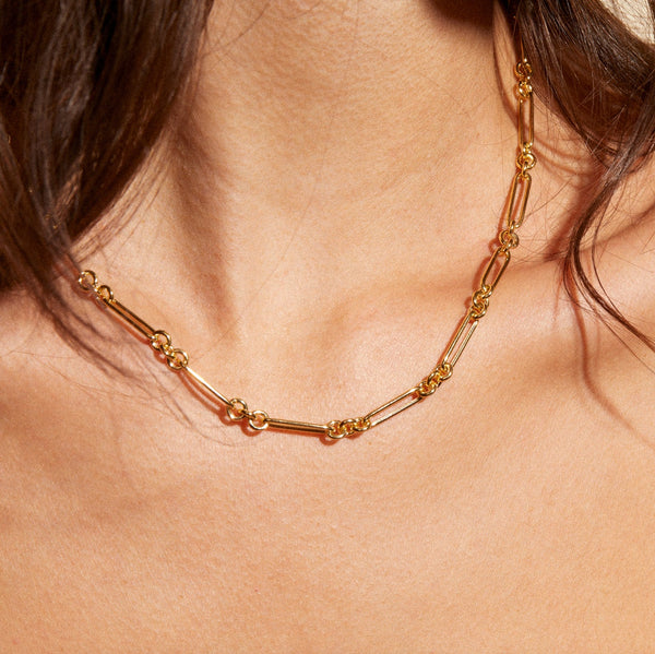 A person is shown wearing the Esmé Paperclip Chain Necklace by zahava, featuring 14k gold with interlocking circular and elongated links. The blurred background highlights the jewelry against their skin.