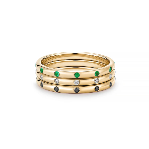 The Eternity Stacker Ring by Kate Collins Jewelry features three 14k gold bands exuding elegance: the top band with green stones, the middle with white, and the bottom with black stones. Polished to perfection, these rings offer a simple yet sophisticated design.