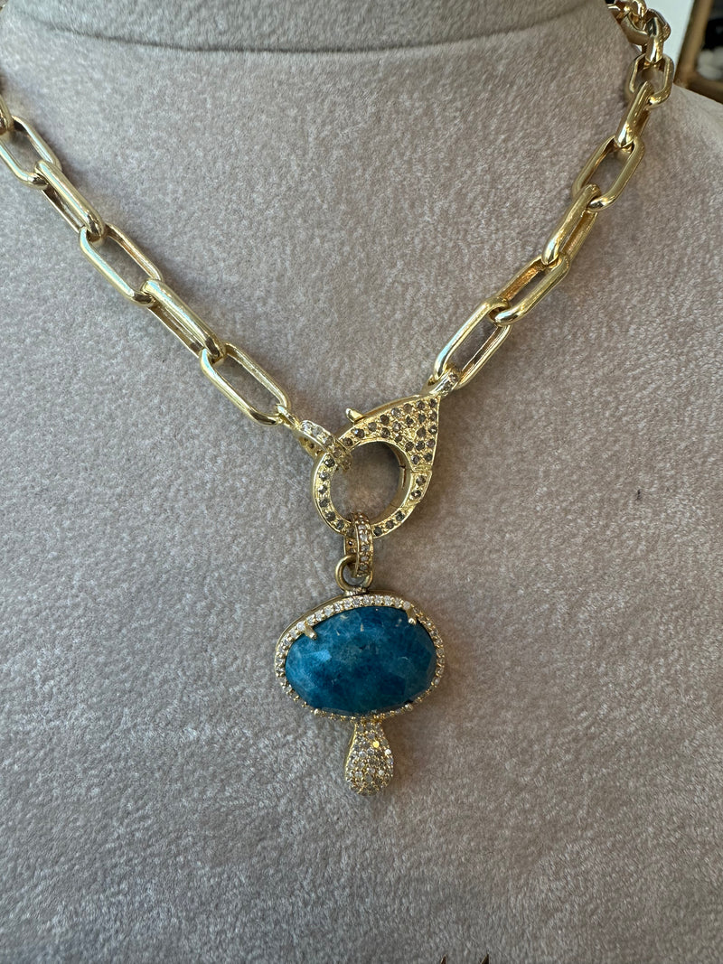 The Woods Blue Diamond Mushroom is a gold chain necklace with a 1.5” blue apatite stone pendant, surrounded by sparkling pave diamonds. The pendant is shaped like a mushroom with an ornate loop, offering unique charm to this exquisite piece.