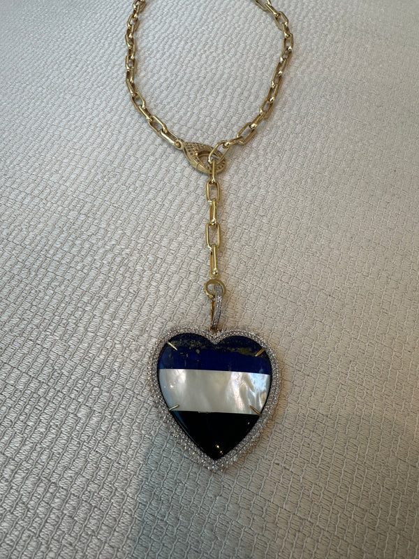 This exquisite gold chain necklace from The Woods showcases the Striped Heart Pendant, adorned with black, blue, and white horizontal stripes and sparkling pave diamonds along its edges. Crafted in 10k gold, it glistens on a textured white background for timeless elegance.