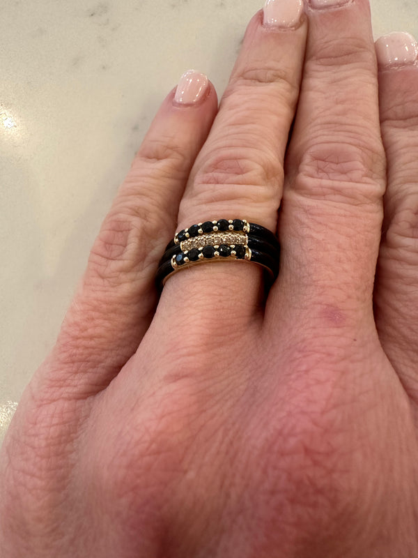 A hand adorned with Rachel Reids stunning Black Enamel and Spinel Band Ring in 14K yellow gold rests elegantly. The neatly manicured nails in light pink polish against a light surface enhance the rings allure.