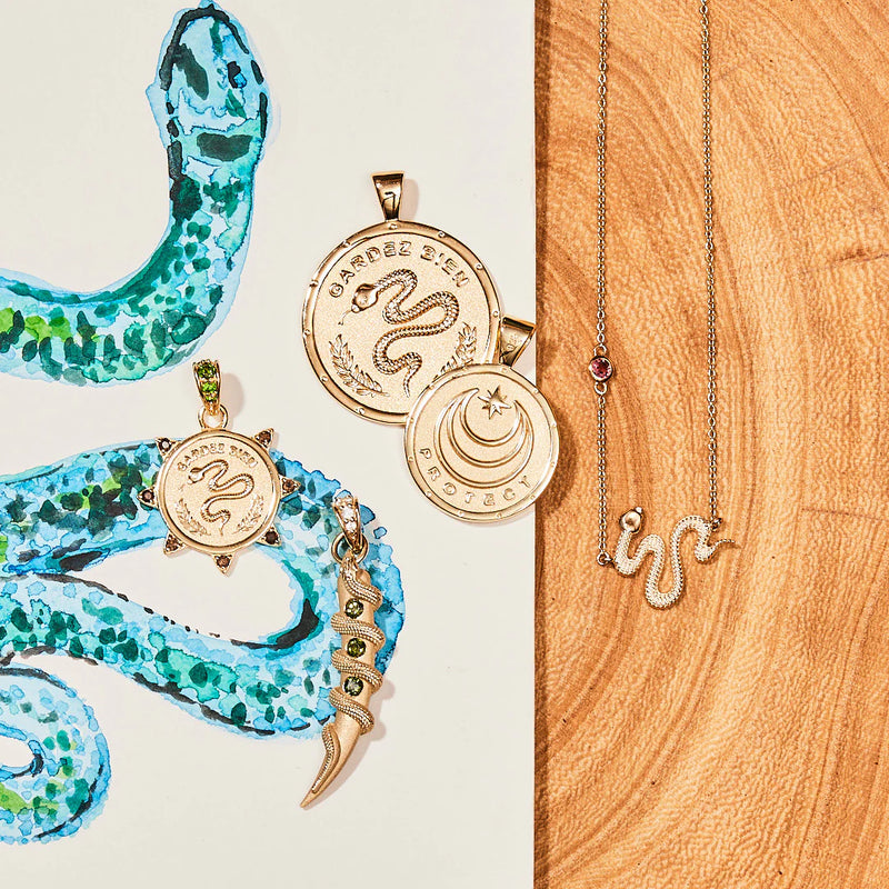 Jane Win’s Protection Coin Pendant—a 14k gold piece—shown with snake motif jewelry and a blue-green watercolor snake, brings unique style and protective symbolism to your collection.