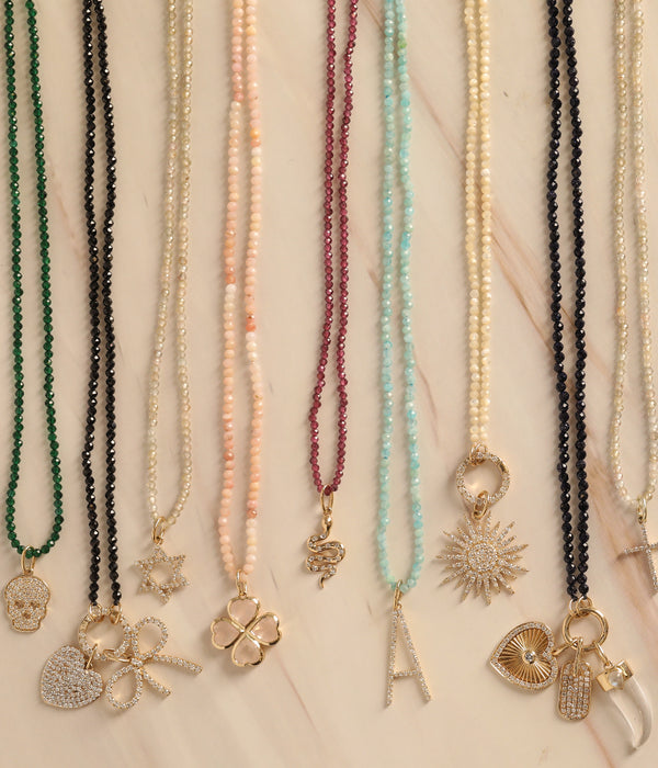 Nine beaded necklaces by Rachel Reid displayed vertically on beige, each featuring a unique gold pendant—including the Gemstone Horn Charm—and a shimmering Moonstone accent.