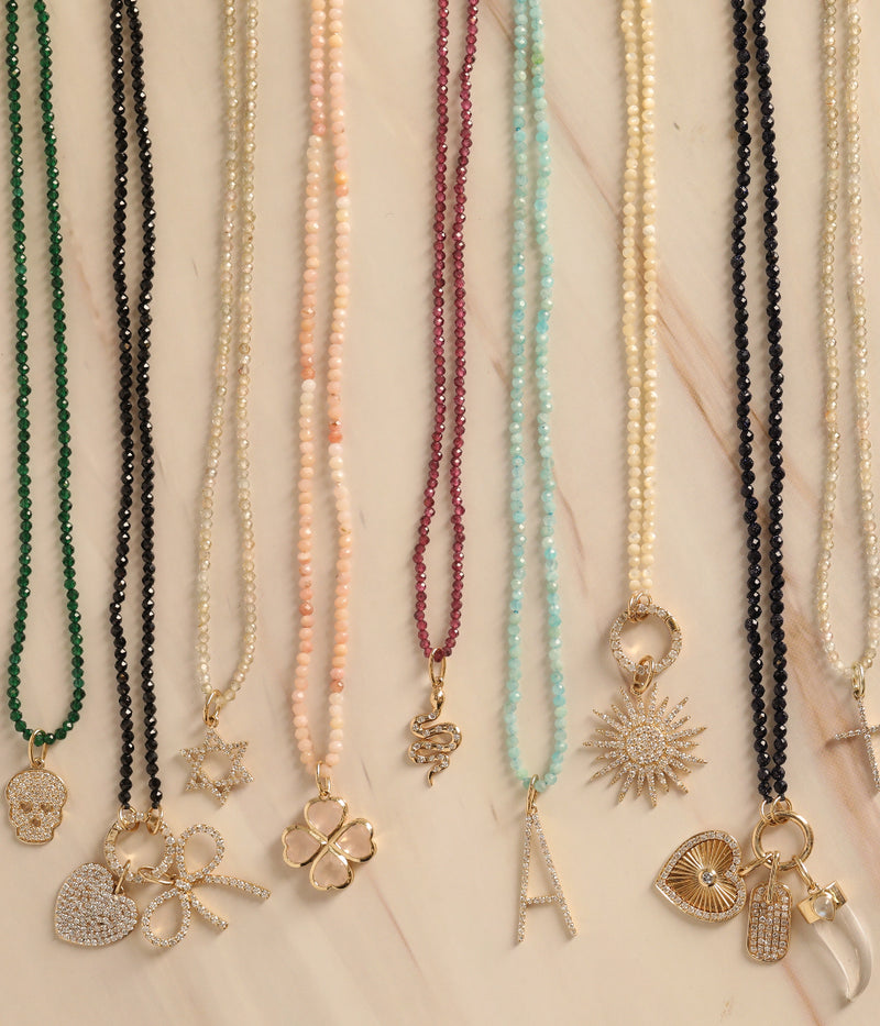 Nine beaded necklaces by Rachel Reid displayed vertically on beige, each featuring a unique gold pendant—including the Gemstone Horn Charm—and a shimmering Moonstone accent.