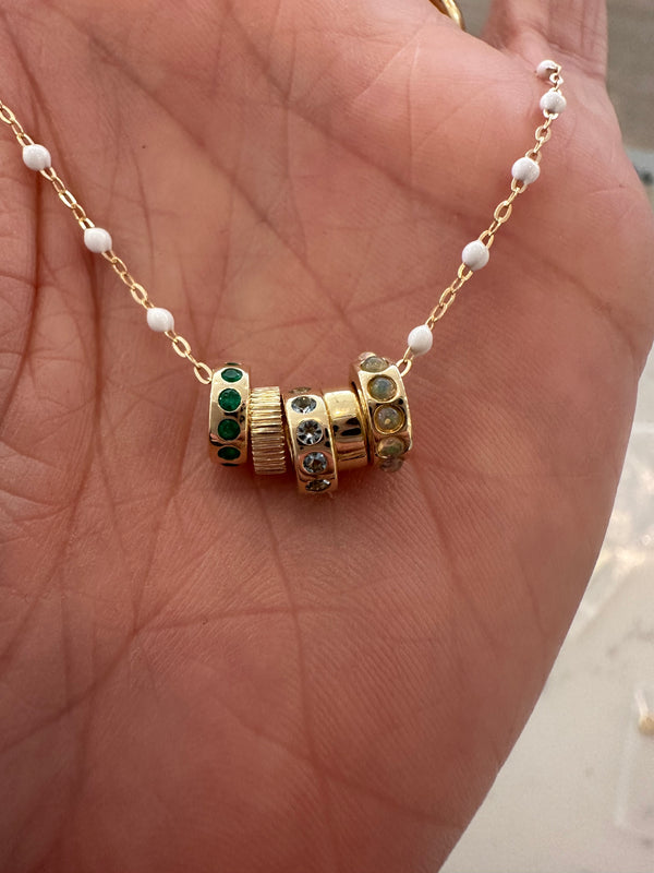 A hand holds Rachel Reids delicate 14k gold chain necklace, adorned with four Gold Wheel Charms set with green, clear, and yellow gemstones—perfect for layering with other pieces.