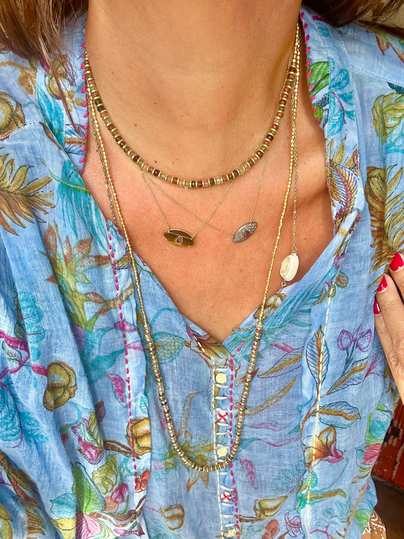 A person dressed in a floral blouse, embellished with an array of multicolored tourmaline necklaces and the sophisticated CHOKER ELLIE by Bohemian Rhapsodie Paris, each showcasing dainty pendants designed to evoke tranquility, ideal for meditation.