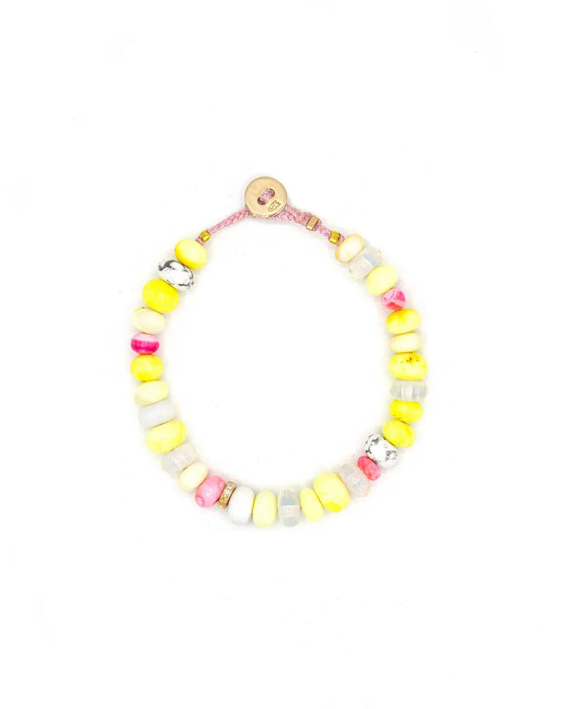 The Scosha Candy Gem Bracelet in Lemonade features chunky yellow, white, pink, and marbled gemstone beads on a pink cord with a round tan button clasp. The bracelet is displayed in a loose circle against a white background.