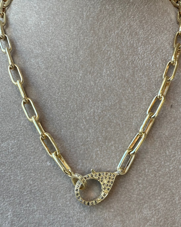 An elongated 17 gold vermeil link chain necklace, named Link chain with diamond clasp from the brand the woods, features a pave diamond clasp centerpiece adorned with small sparkling stones, showcased on a fabric background.