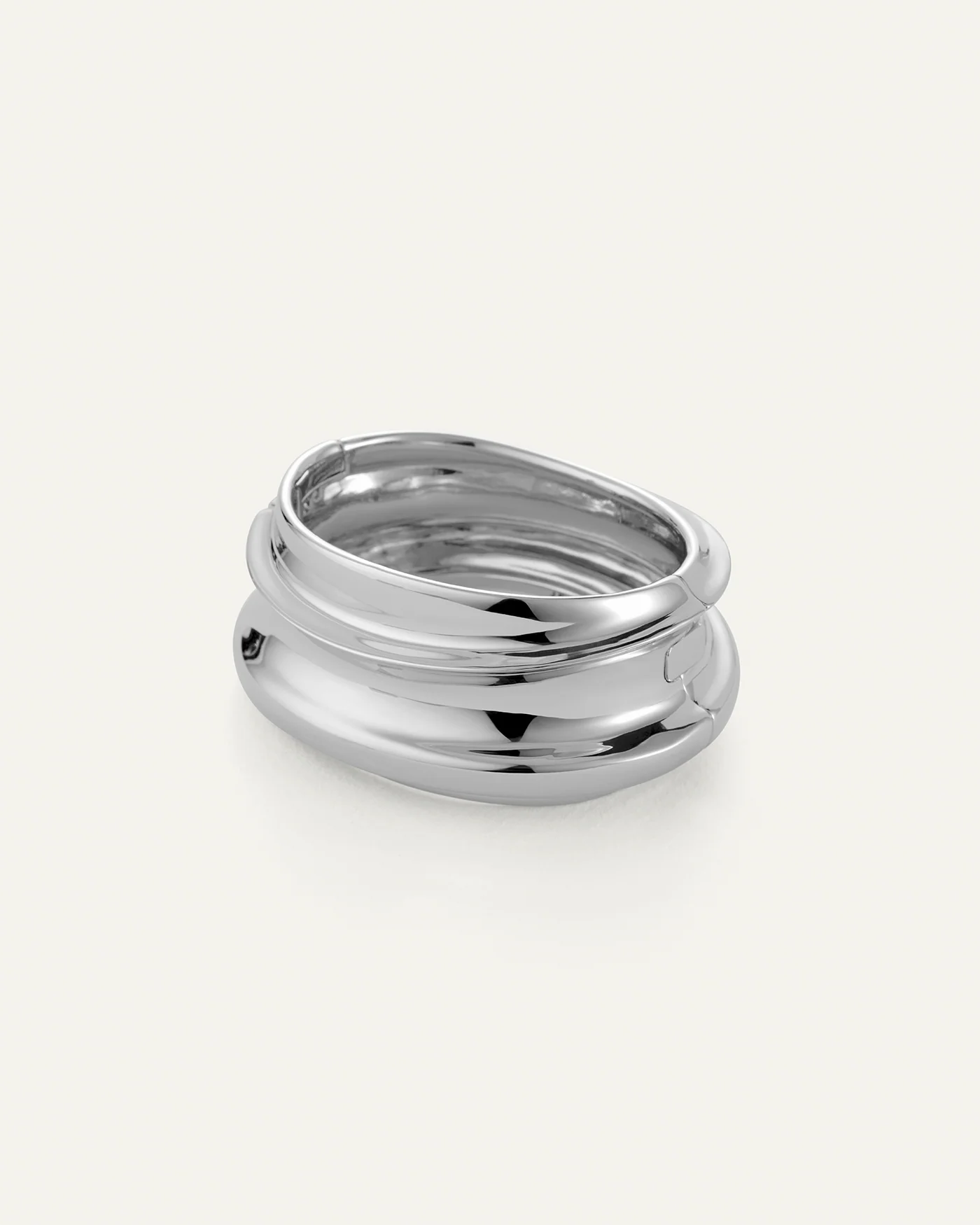 The Jenny Bird Mega Lennon Bangle is a shiny, silver statement piece with a chunky, smooth, wavy design and stacked layers, showcased on a plain white background.