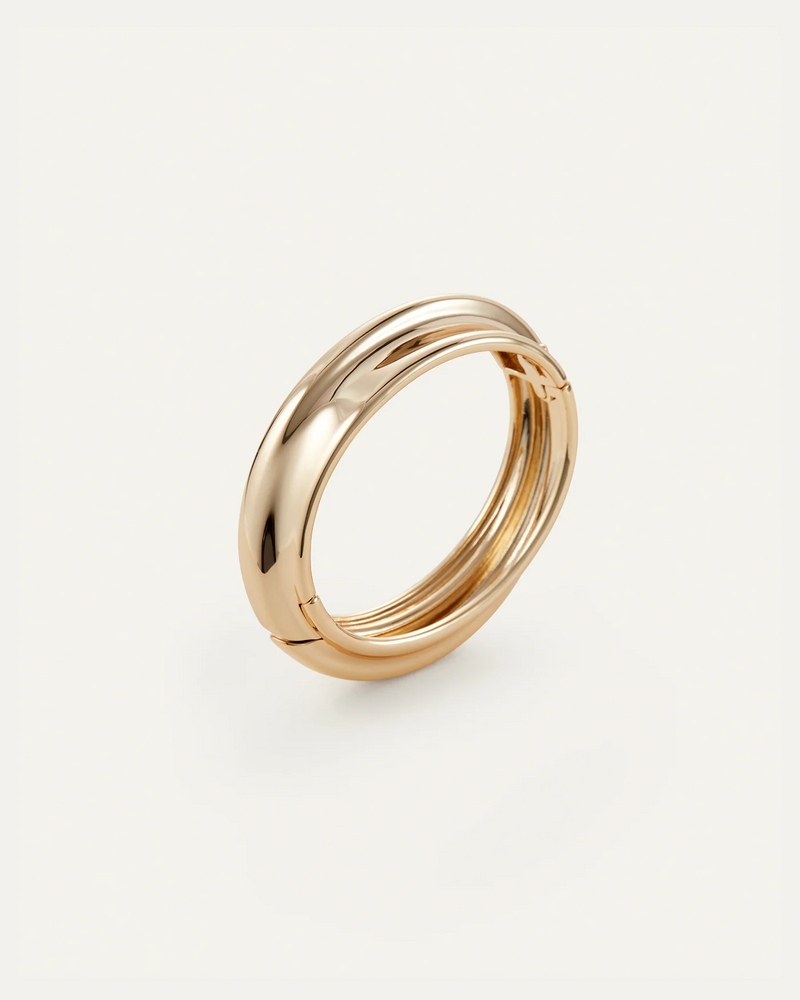The Jenny Bird Lennon Bangle, featuring a shiny gold-tone dipped interlocking double-band design, is displayed against a plain off-white background.
