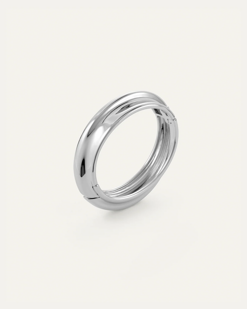 The Lennon Bangle by Jenny Bird is a shiny, silver, circular metal accessory with a smooth, organically-shaped surface, shown on a plain white background.