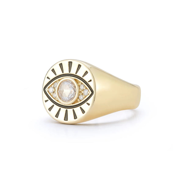 The Protection Signet Ring by Kate Collins Jewelry is a 14K gold piece with an eye talisman design, featuring a central rose-cut diamond surrounded by smaller stones on a flat, round surface accentuated with engraved black lines radiating around the eye.