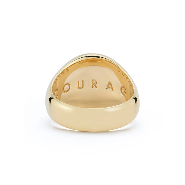 The Courage Signet Ring by Kate Collins Jewelry showcases a 14k gold design with COURAGE engraved inside, featuring a smooth polished finish, lion symbols on the sides, and diamond eyes for added brilliance.