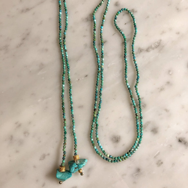 Intertwined on a marble surface, Bohemian Rhapsodie Pariss KEVIN Lariat necklaces showcase their distinct personalities: one features larger stone pendants with gold-plated caps, while the other is a simple strand of small beads.