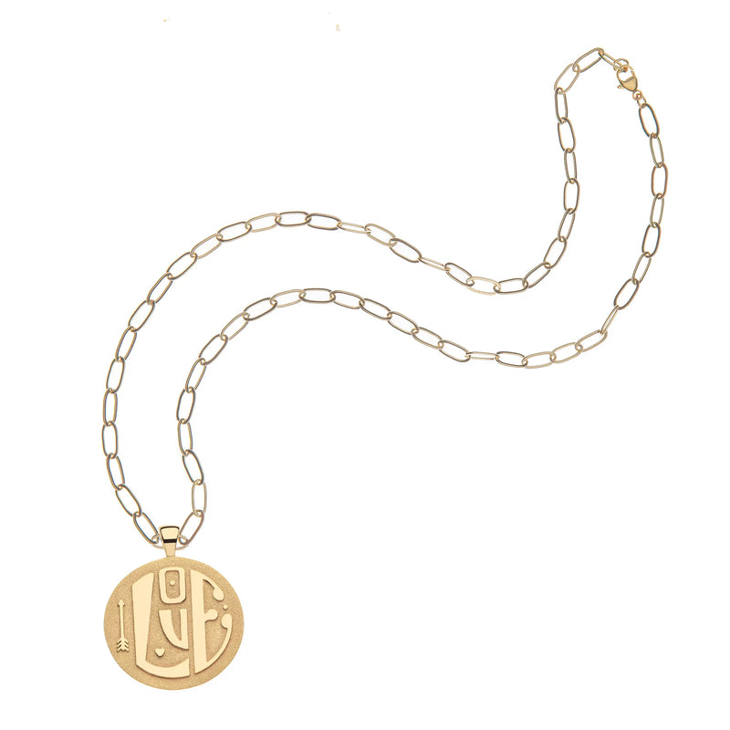 The Jane Win Jumbo LOVE Pendant is a 14k gold plated necklace featuring intricate circular patterns on an engravable pendant. The chains elongated oval links enhance its sleek, elegant look against a white background, adding a personal touch to any outfit.