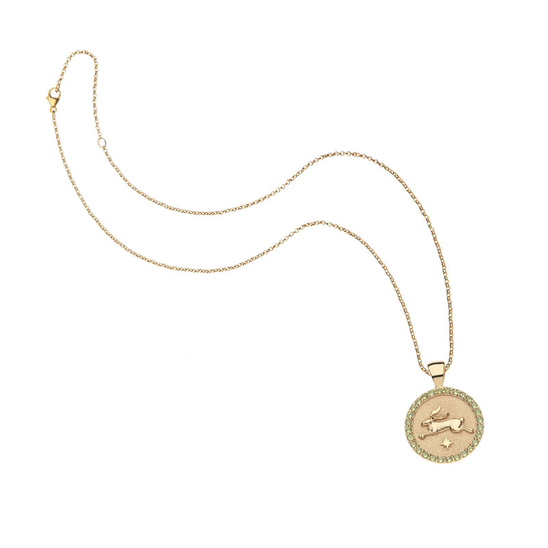 The LUCKY Rabbit JW Small Embellished Pendant Coin by Jane Win is a delicate gold necklace with a sterling silver pendant, raised Capricorn zodiac symbol, and surrounded by small Peridot stones.