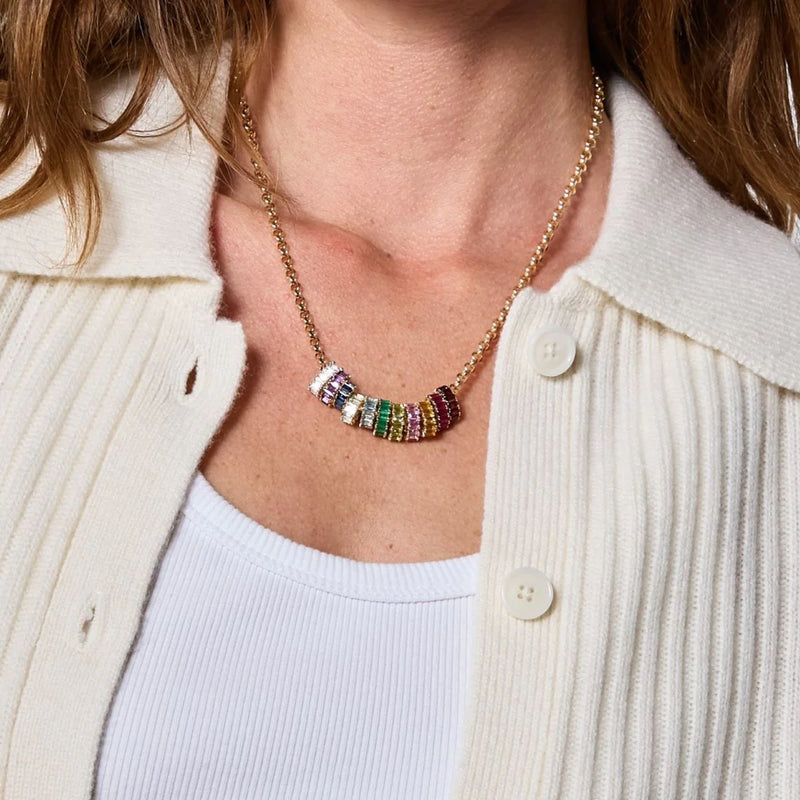 Adorned with an Adina Reyter Emerald Baguette Big Bead 14k gold necklace featuring pink, green, yellow, and white beads, a person pairs this with a cream cardigan over a white top.