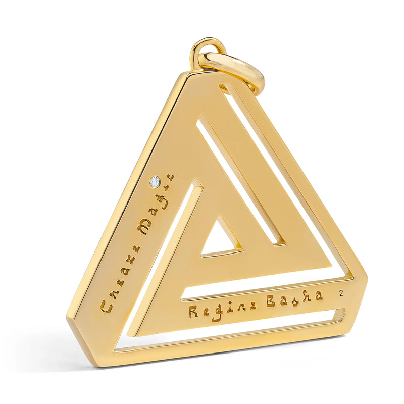 The Large Abracadabra Triangle Series 4 necklace by Aaron Basha features a gold triangular pendant with an empowering geometric cut-out design, engraved with Chase Magic and Regina Basha, adorned with a small gem and finished in reflective 18K gold plating.