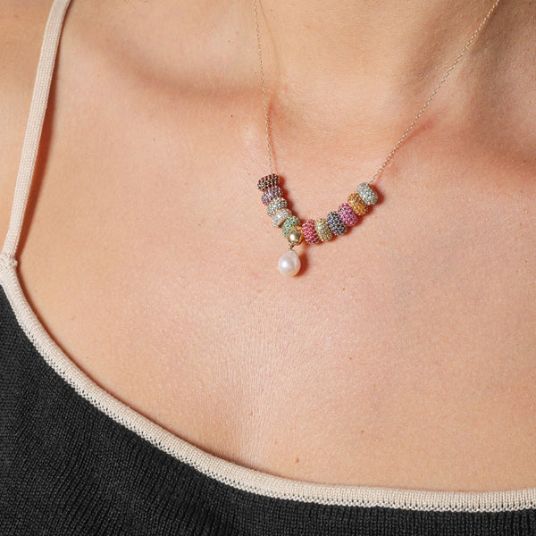 A person adorned in a 14k gold chain necklace with vibrant beaded segments featuring Adina Reyter's Wide Pavé Blue Sapphire Mini Bead, paired with a delicate amethyst birthstone pendant, shimmering just above a stylish black and beige tank top.