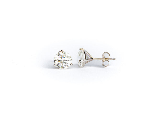 The Monarch Market Lab Grown Studs feature pear-shaped diamonds in a simple silver prong setting. One earring faces upright, revealing the diamonds front, while the other lies on its side, showing the back and post. Both rest on a white surface.