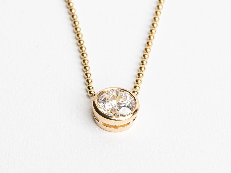 The Monarch Market Lab Grown Large Gold Bezel Necklace features a gold beaded chain and a round, faceted gemstone set in a luxurious gold bezel, sparkling beautifully against a plain white background.