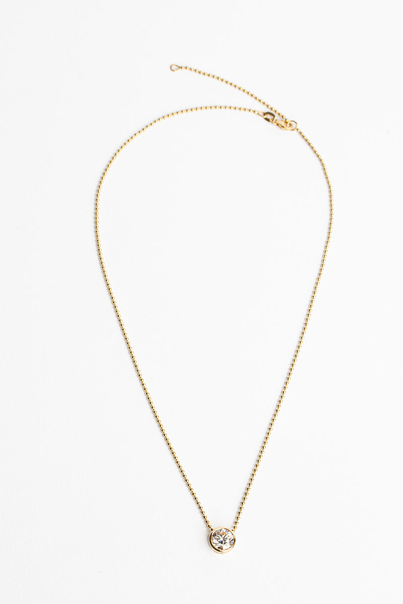 A Lab Grown Large Gold Bezel Necklace by Monarch Market, featuring a delicate gold chain with a single round diamond pendant, is displayed against a plain white background.