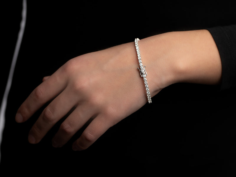 A hand elegantly adorned with the Monarch Market Lab Grown Tennis Bracelet sparkles against a dark background, highlighting its simplicity and elegance.