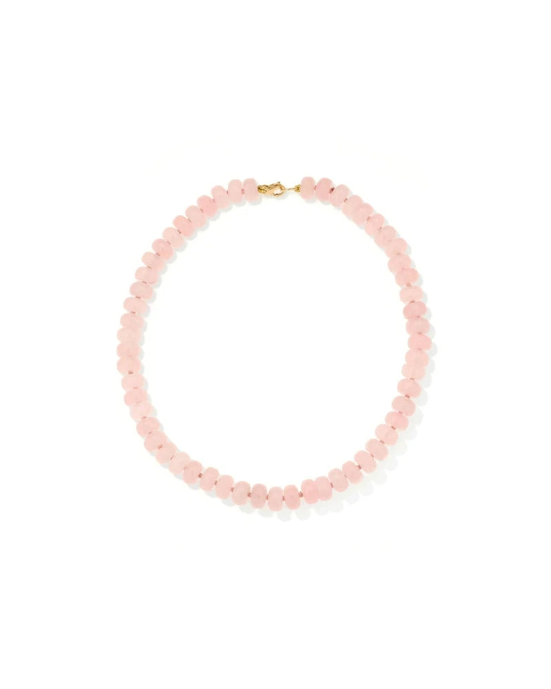 The Spring into Pink Gemstone Necklace by Adina Reyter showcases round, pale pink rose quartz beads and a small gold clasp, arranged in a circle on a white background. This limited edition piece exudes feminine elegance.