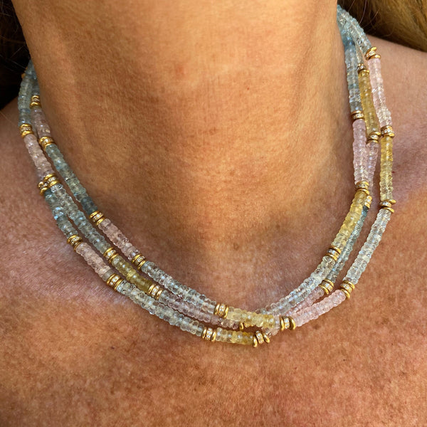 The NOTO necklace by Bohemian Rhapsodie Paris features a close-up of a neck adorned with three strands of small, translucent beads in blue, pink, and yellow. Exquisite 18K fine gold bands are woven throughout, offering Baroque elegance reminiscent of a Sicilian town.