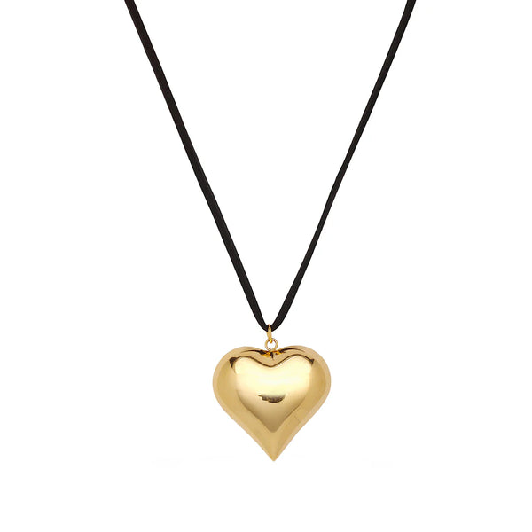 The Oiya Gold Heart Suede Necklace features a shiny gold heart pendant elegantly hanging from a black suede cord, set against a plain white background to highlight its exquisite handmade jewelry craftsmanship.