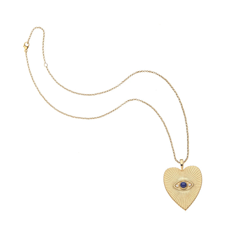 The Jane Win PROTECT Eye On Your Heart Pendant is a gold chain necklace featuring a heart pendant with a sunburst pattern and a central blue evil eye design inspired by lapis stones.