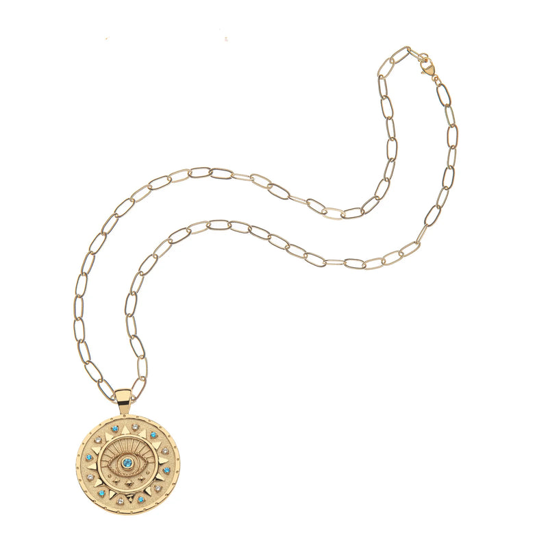 The Jane Win PROTECT Ancient Eye Pendant is a limited edition gold necklace featuring an intricate circular evil eye design with a central blue motif, sparkling blue sapphires, and crystal accents on an elongated link chain.