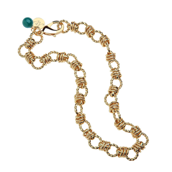 The Jane Win Rings of Gold Chain with Malachite Bead is a chunky gold-plated necklace with circular links, a green malachite bead charm, and a small gold tag near the clasp, shown on a white background.