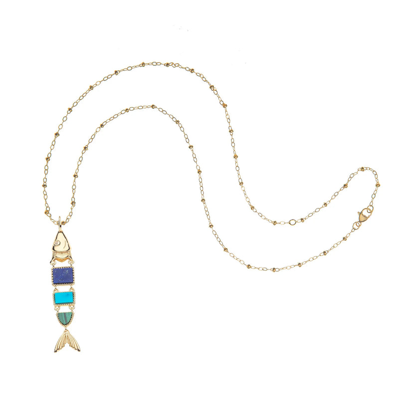 The Jane Win STRONG Carpe Diem Fish Pendant is a gold chain necklace with a fish-shaped, gold-plated pendant. It features a gold head and tail, plus three blue and turquoise rectangular stones in the body for a vintage look.