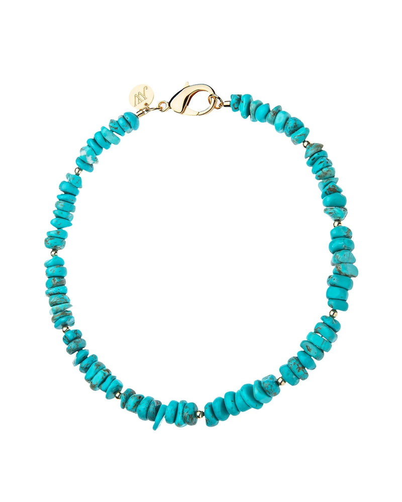 The Jane Win Turquoise Natural Beaded Necklace features irregular turquoise stones, small metallic spacers, a gold-plated brass clasp, and a round engraved charm—an ideal summer accessory.