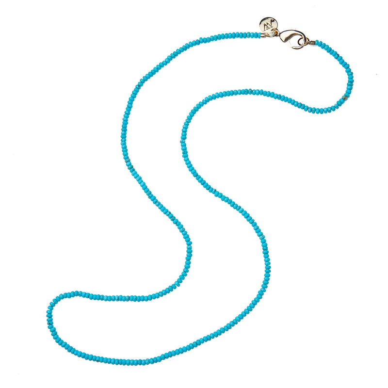 The Jane Win Double Wrap Diamond Cut Beaded Necklace in Turquoise features small, diamond-cut beads with a silver clasp and circular charm, elegantly displayed against a white background.