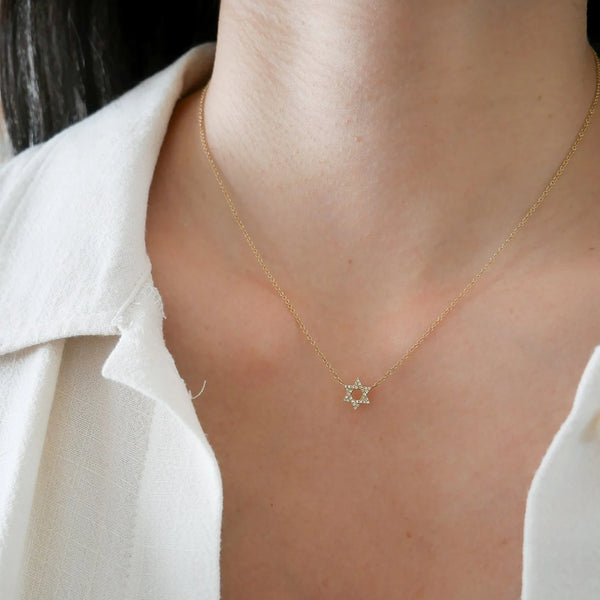 A close-up of a person wearing the Diamond Star Of David Necklace by ef collection, showcasing its ethically sourced diamond pendant. The person is dressed in a white shirt, highlighting the shimmering pavé diamonds on their upper chest, while the background stays tastefully blurred.