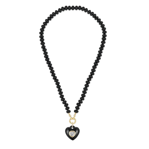 The Black Onyx Rondelle Bead Necklace by Kate Collins Jewelry features black beads forming a circular loop, a heart-shaped pendant with a central gem, and is elegantly finished with a 14K gold clasp and small attachment for timeless sophistication.