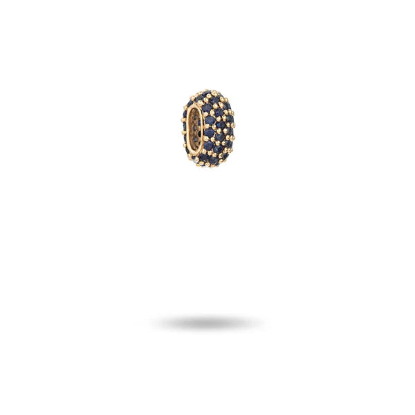 The Wide Pavé Blue Sapphire Mini Bead by Adina Reyter, crafted in 14k gold and encrusted with vivid dark blue sapphires, elegantly floats against a plain white background, casting a delicate shadow below. Its captivating design makes it an exquisite choice for those seeking the allure of their birthstone.