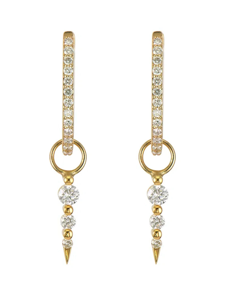 Medium Sari Dagger Charm by Three Stories Jewelry are vintage-inspired gold hoop earrings in 14K yellow gold. They feature small clear gemstones on the hoops, a dangling section with three clear stones, and a gold spike, exuding an elegant and shiny allure.