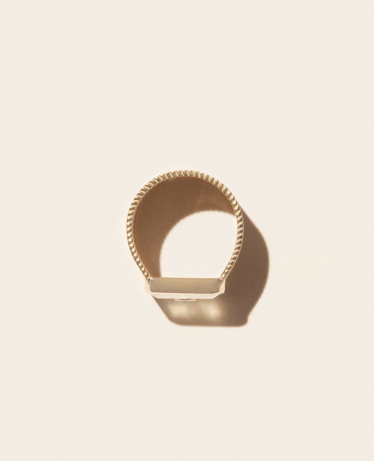 The Pascale Monvoisin ANTON N°2 MOONSTONE Ring, a minimalist yellow gold ring with a rope-like texture, is displayed on a light beige background, casting a soft shadow.